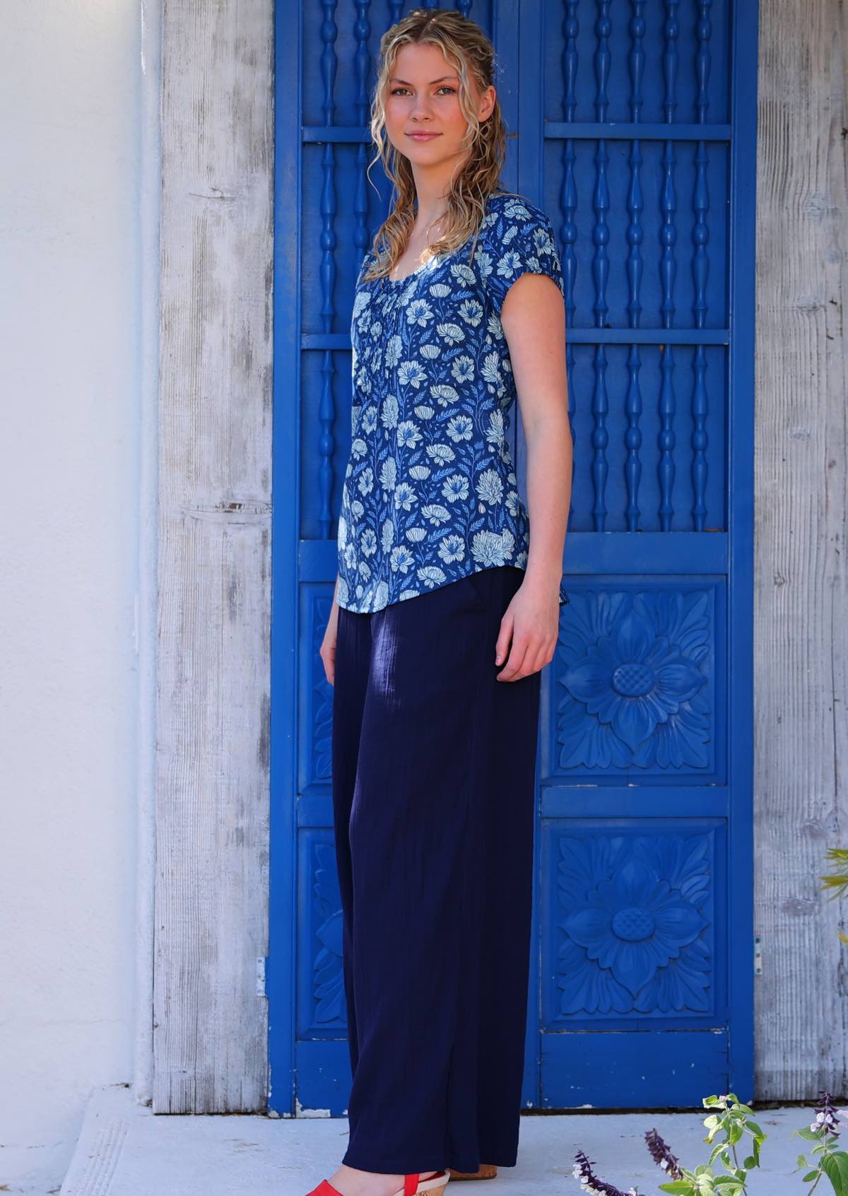 Model standing in front of blue door wearing 100 percent cotton navy floral blouse with scoop neck paired with wide leg navy pants