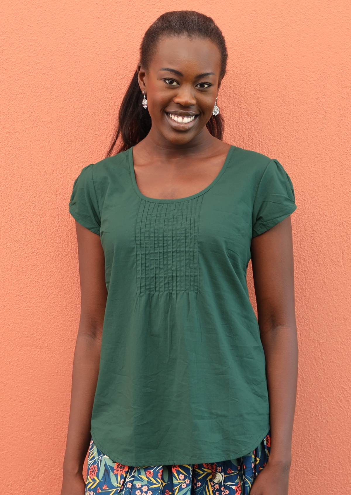 Smiling model pairs green short sleeve cotton top with silver earrings.