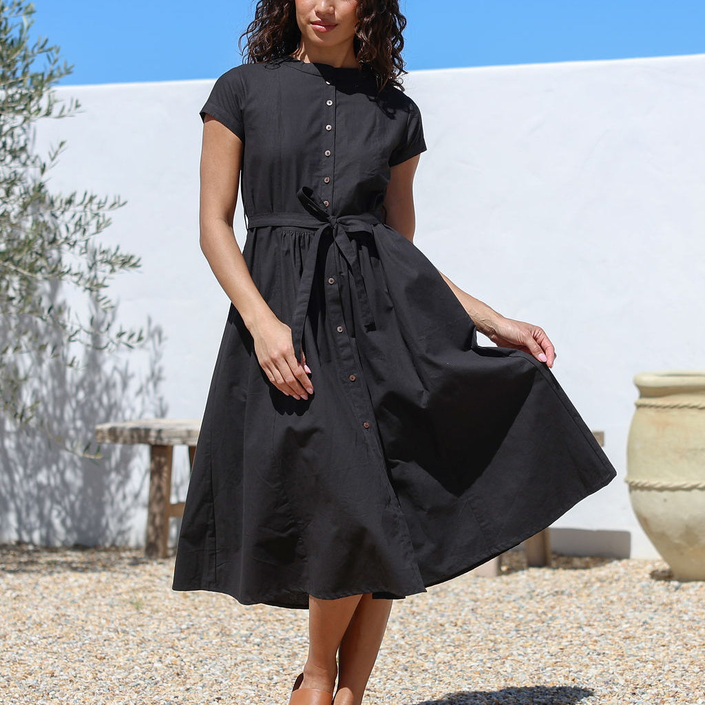 Woman wearing a black cotton retro style dress standing outdoors with a white wall