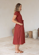 Woman with her hands in pocket wears a retro style, button through rust-colored dress standing in a room with neutral decor