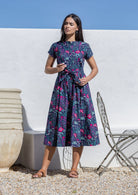 Woman wearing a navy floral dress standing against a white wall with a blue sky.