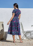 Woman wearing a floral  cotton sundress standing outdoors against a white wall.