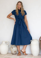 Woman poses in 100% cotton retro button through dress with waist tie, high round neckline and mandarin collar