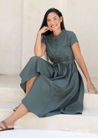 Woman in a moss green 50's style cotton dress sitting on steps with a neutral background