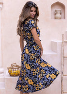 Side pose of model wearing a yellow, green, grey floral cotton dress with detachable waist tie, short sleeves and high mandarin collar.