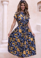 Model wears mid length cotton dress with yellow, green and grey floral print on black base.