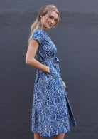 Woman poses in cotton midi length dress in blue based floral print with her hand in hidden side pocket