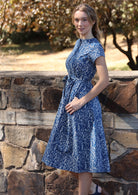 Woman wears cotton 50's style midi length dress with cap sleeves and waist tie, with thumb hooked in side pocket