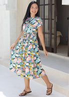 Woman standing sideways in cotton 50's style midi length dress in pastel colours with waist tie