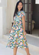 Woman standing in cotton 50's style button through dress in pastel colours with cap sleeves and waist tie