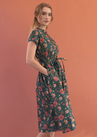 Side pose of model wearing a button through cotton dress with tieable waistband and hands in pockets.