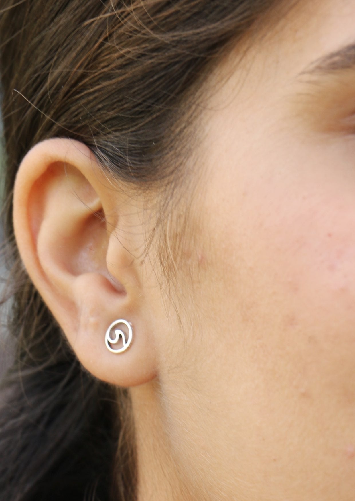 Close-up of an ear wearing a silver circular studs with cutout wave design