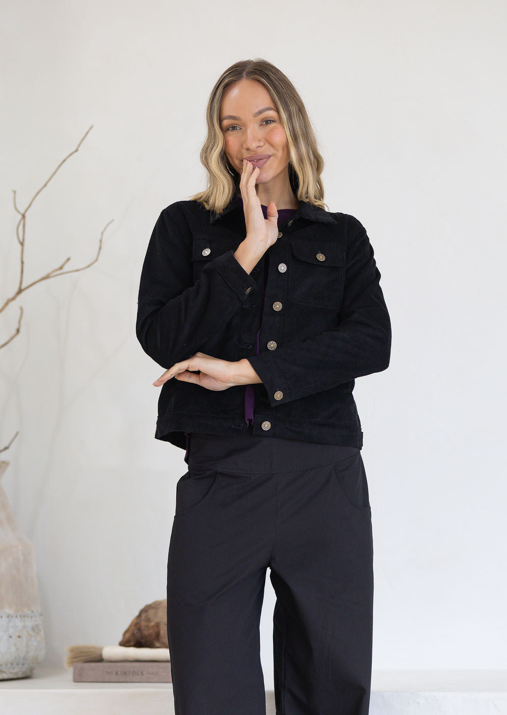 Woman wearing a black corduroy jacket and black cotton pants against a white background