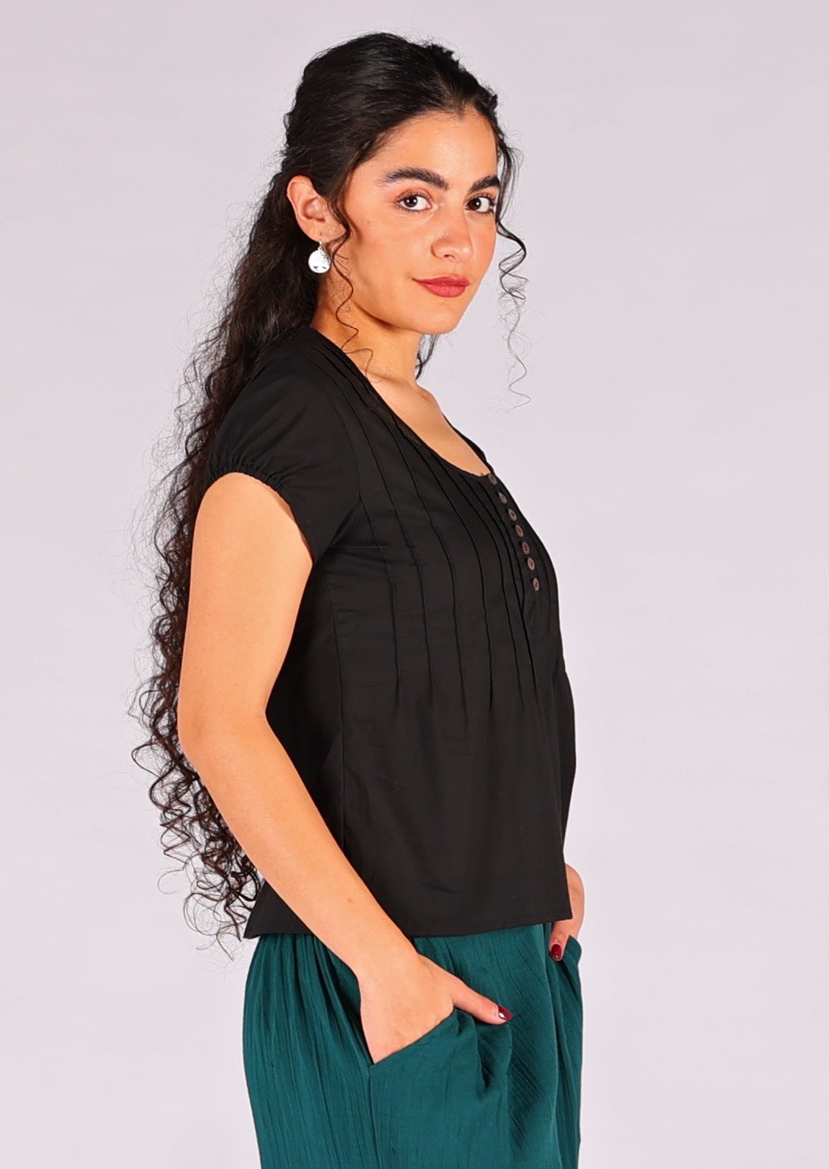 Model stands with her side to the front in black 100% cotton cap sleeve top with elastic in the trim