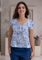 Woman wearing a white based blue floral print cotton top in an indoor setting.