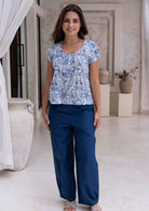 Woman wearing a white based blue floral print cotton top with dark pants.