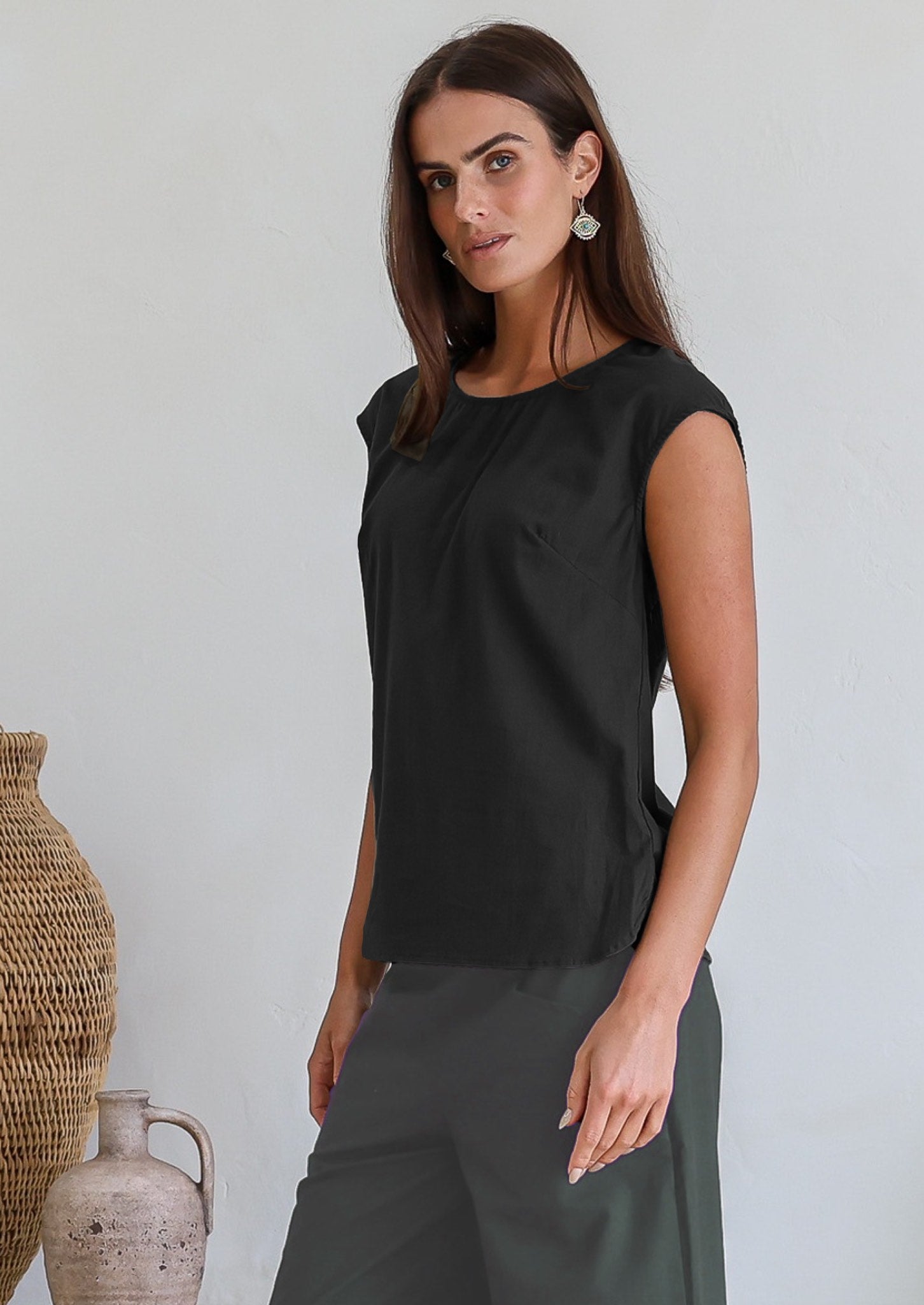 Woman wearing a black cotton sleeveless top with a high round neckline and bust darts