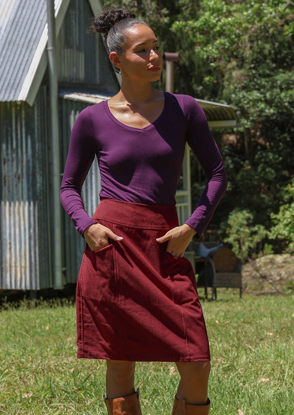 Woman wearing cotton corduroy skirt in deep, luxurious, and intense red-purple hue with both hands in pockets