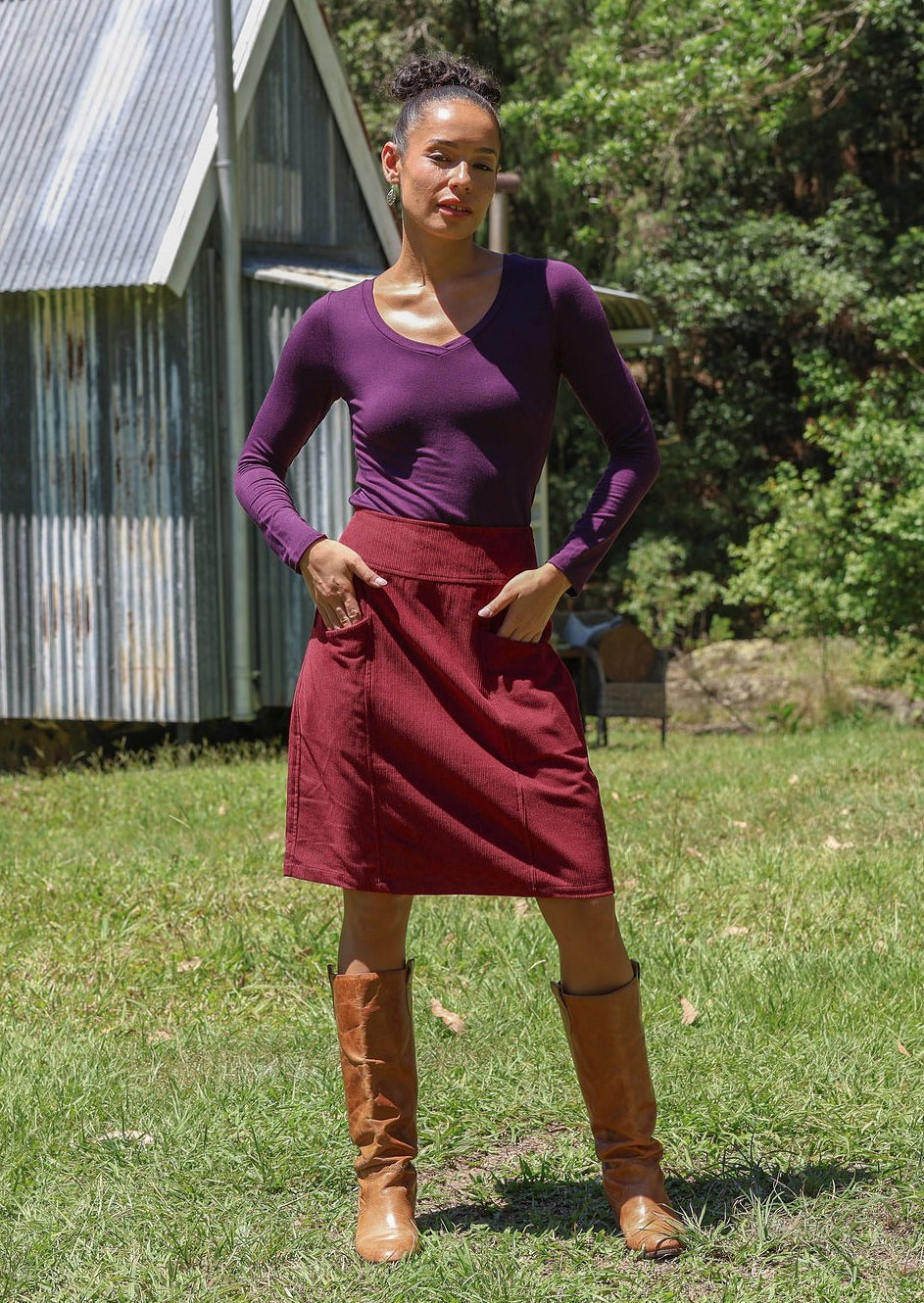 Woman wearing a basic top and cotton corduroy skirt in deep, luxurious, and intense red-purple hue with boots standing outdoors.