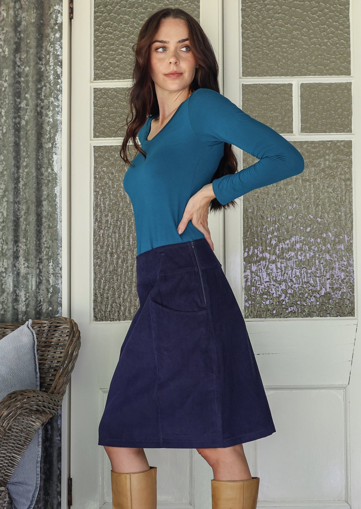 Woman wearing a basic top and corduroy skirt with tan knee-high boots indoors.