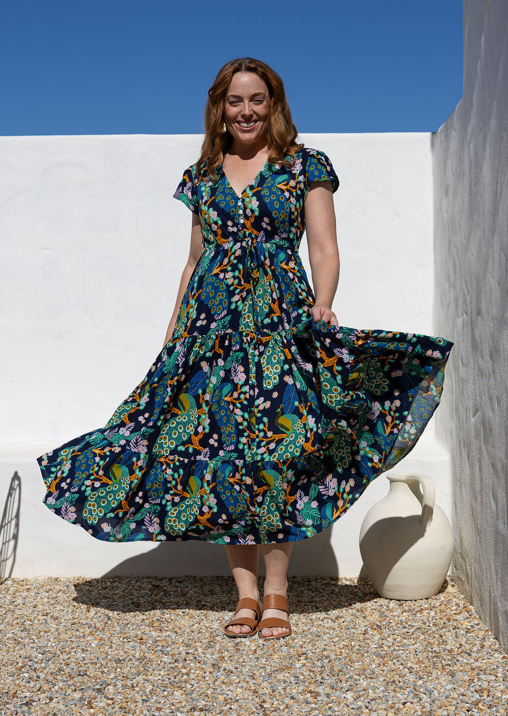 Woman swirling the skirt of her rayon maxi dress with a buttoned bodice, cap sleeves and shoestring ties to cinch the waist