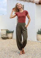 Woman in a terracotta basic top and green cotton pants with wide flat front waistband shirred at the back and cuffed ankles