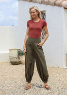 Woman standing with one hand in pocket wearing 100% cotton wide legged olive green cotton pants with cuffed, buttoned ankles and pockets