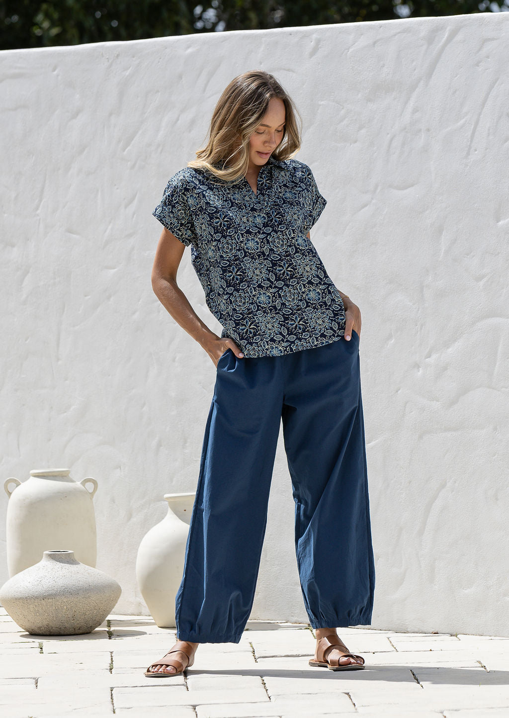 Woman wearing a navy blue based relaxed fit, shirt style floral cotton top with plain pants.