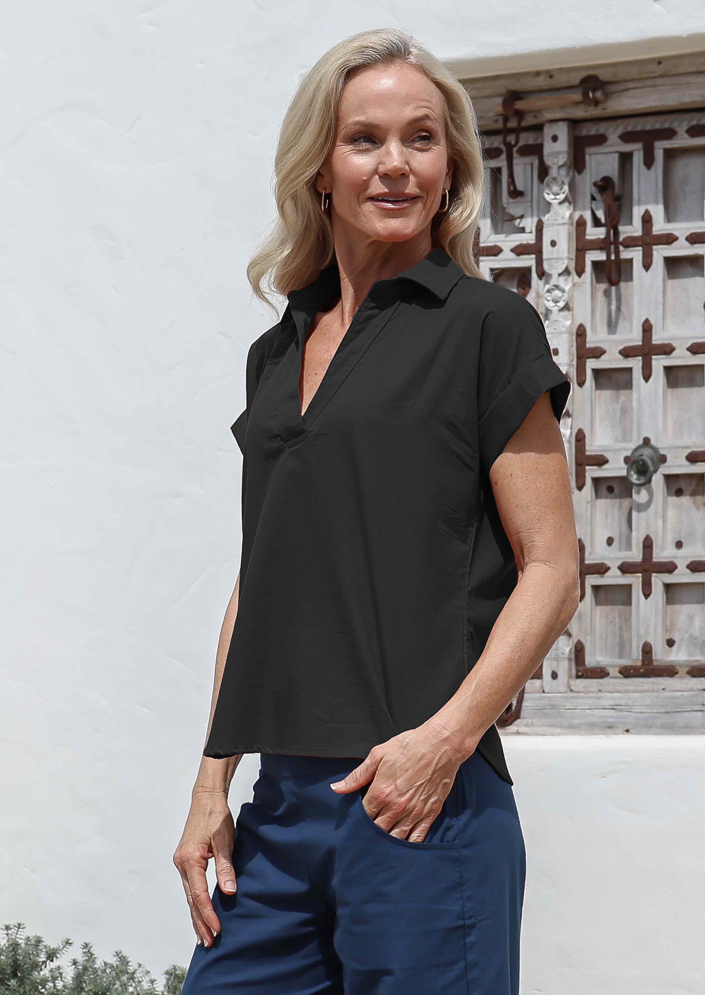 Woman stadning side on wearing a black cotton short-sleeve relaxed fit top with a collar and blue pants