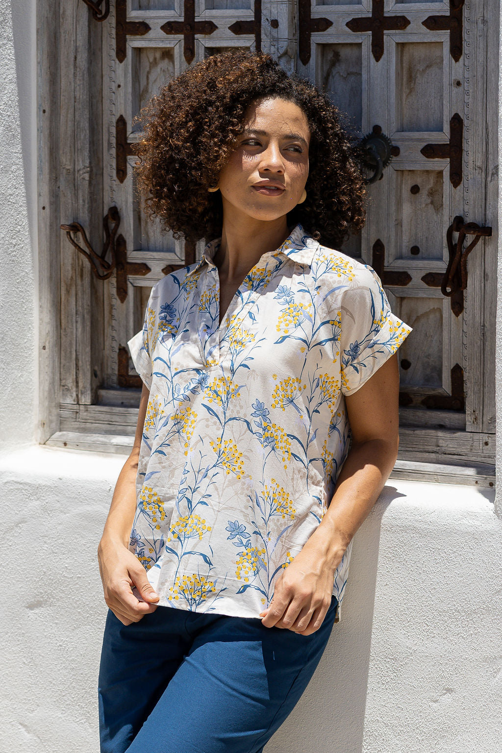 Woman wearing a neutral based relaxed fit, shirt style floral cotton top with blue plain pants.