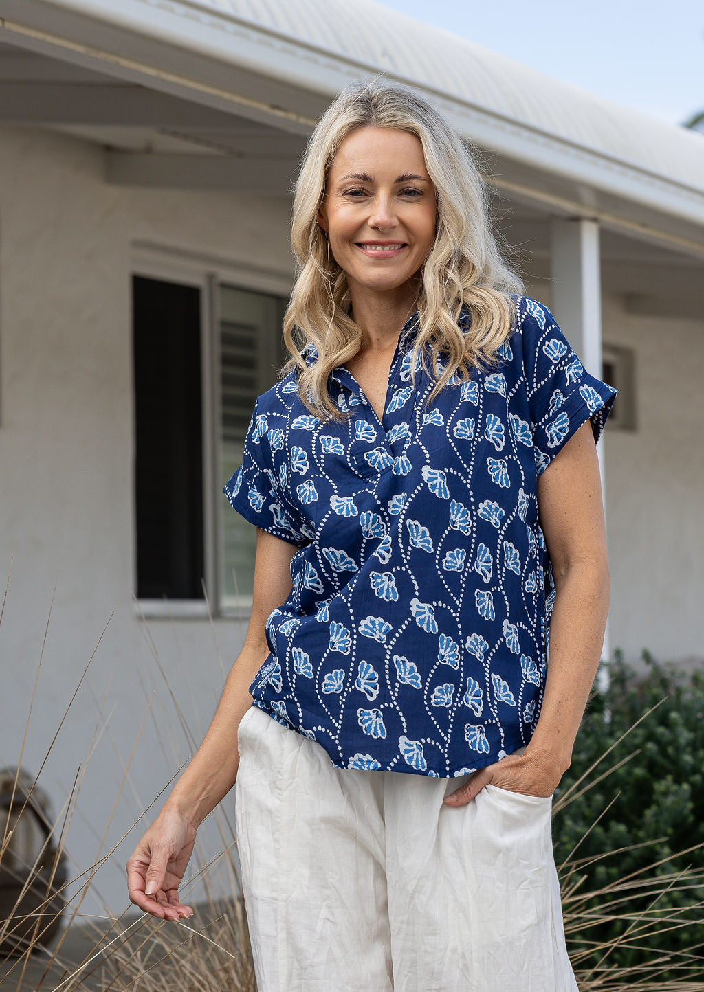 Woman wearing a navy blue based relaxed fit, shirt style floral cotton top with plain pants.