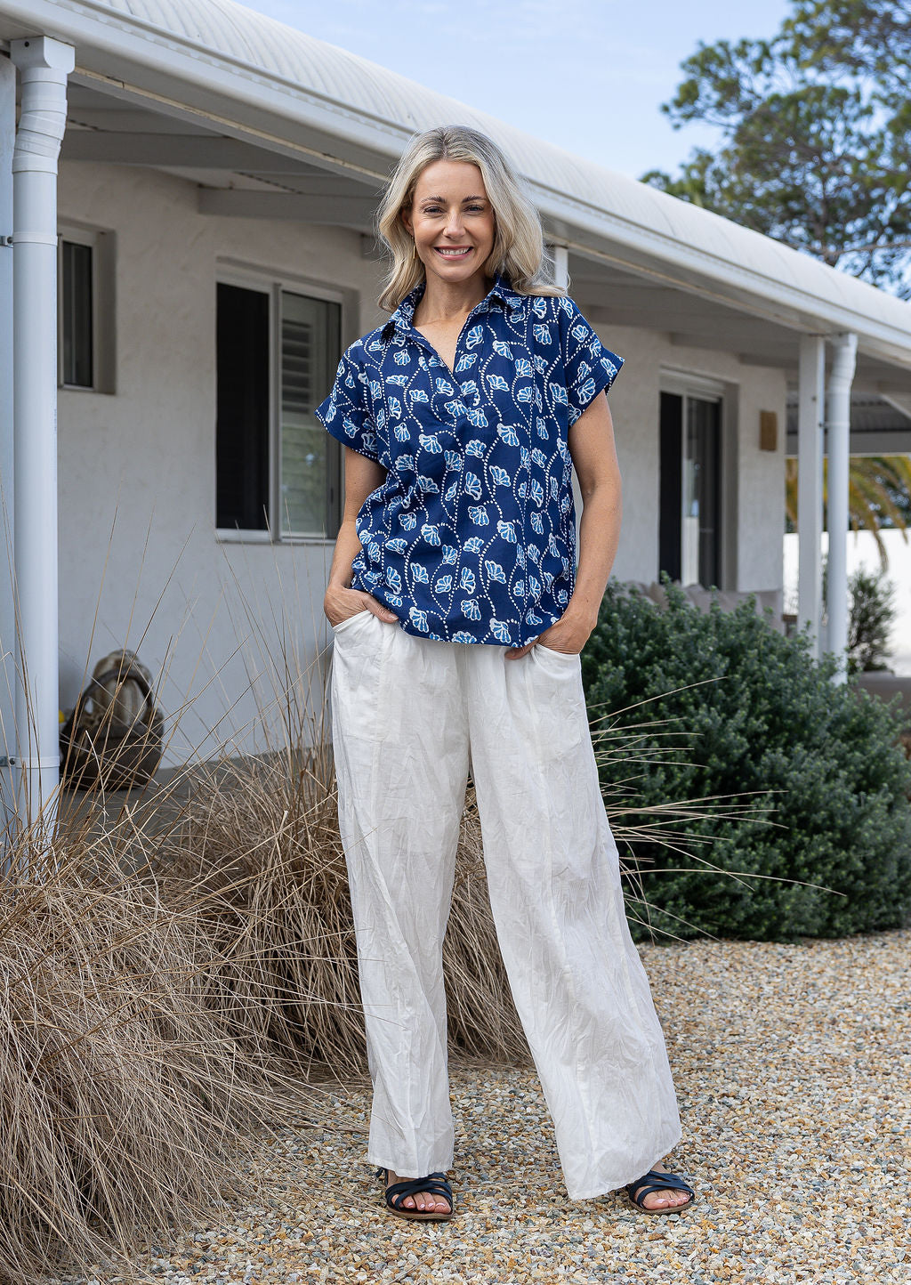 Woman wearing a floral 100% cotton top with short folded cuff sleeves paired with plain white pants