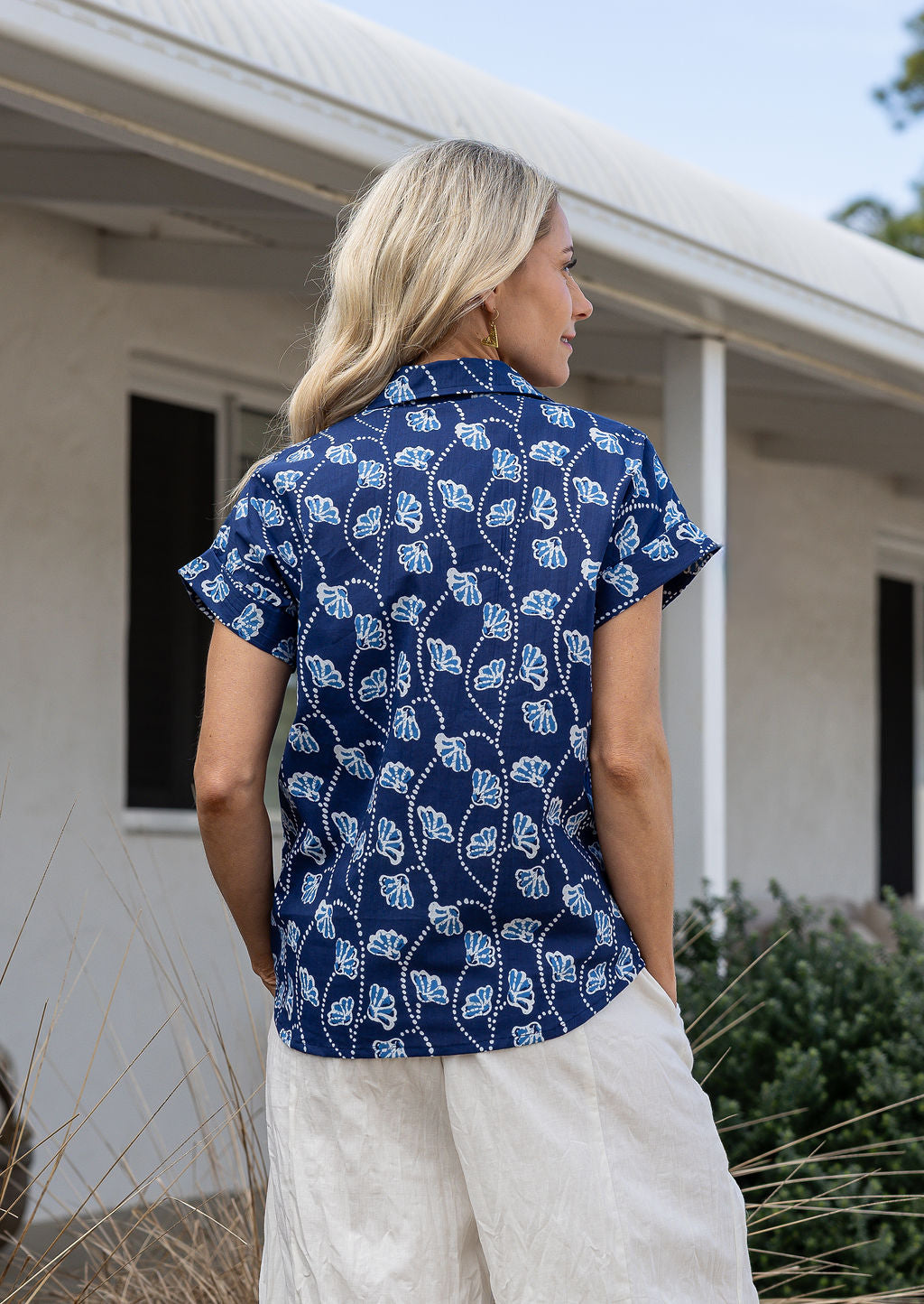 Woman standing backwards wearing a floral cotton top with short folded cuff sleeves, collar and V neckline