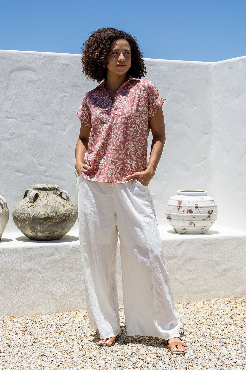 Woman wearing a rose pink based relaxed fit, shirt style floral cotton top with white plain pants.