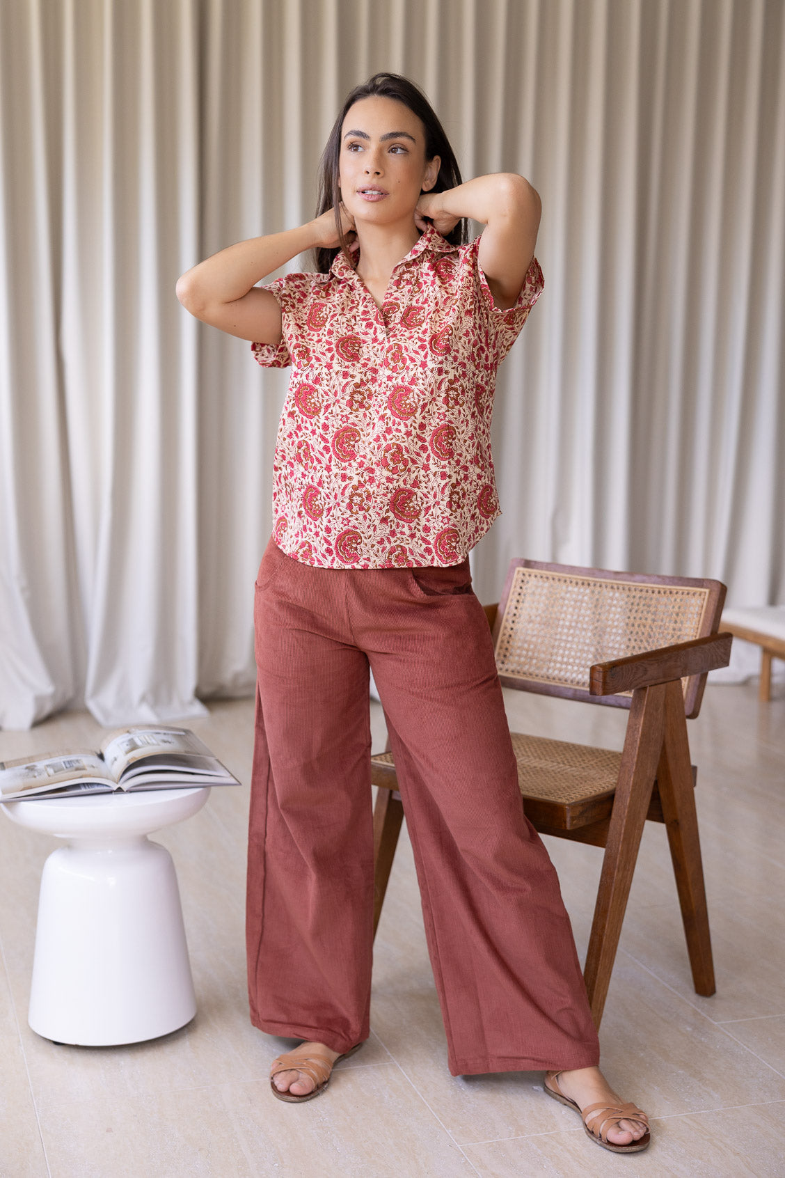 Woman stands wearing a gentle cream based floral cotton top with short folded cuff sleeves, collar and V neckline