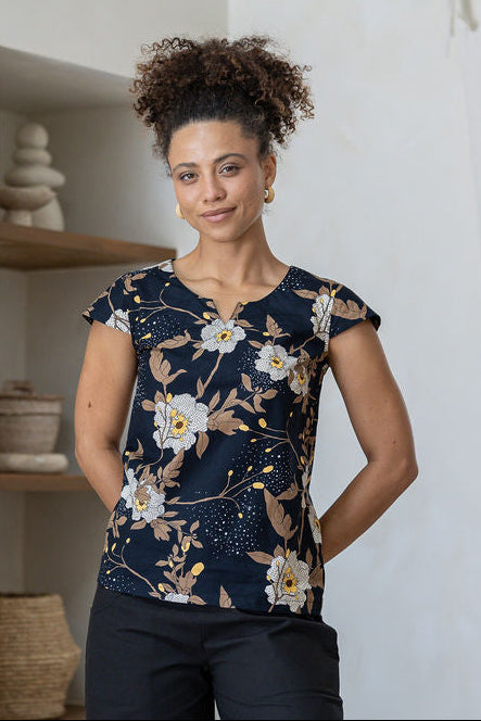 A woman poses in a cap-sleeved cotton tailored top with black based floral print