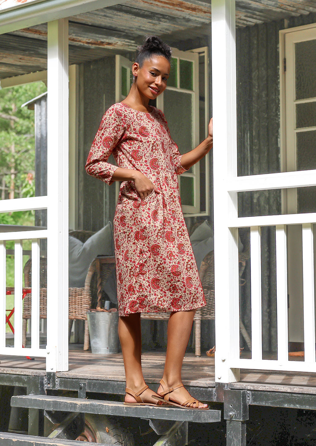 Woman standing sideways wearing a knee length sundress with cream based floral print