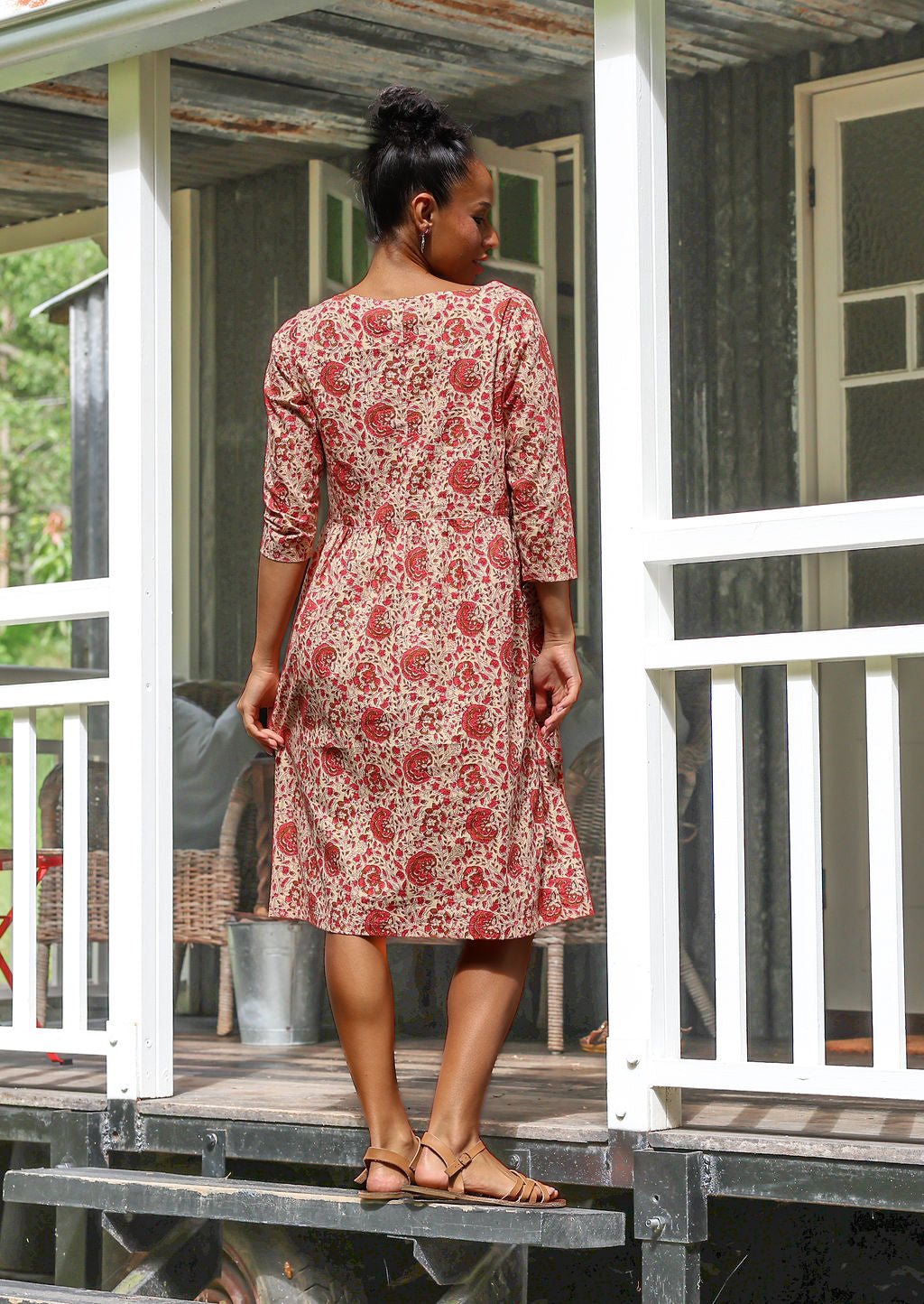 Woman standing backwards wearing a knee length sundress with cream based floral print
