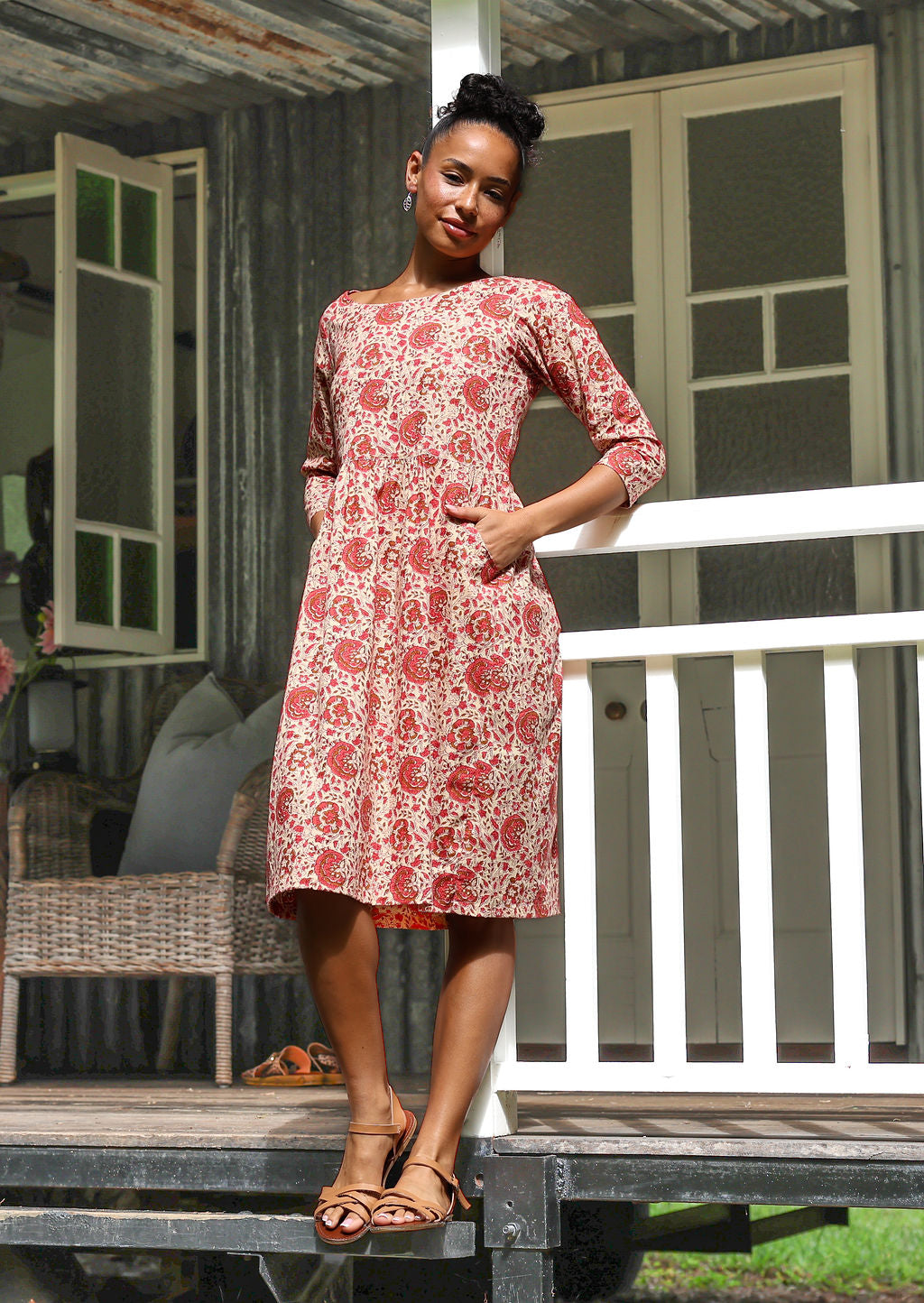 Woman in cream based floral print, knee length sundress with sleeves, with hand in pocket