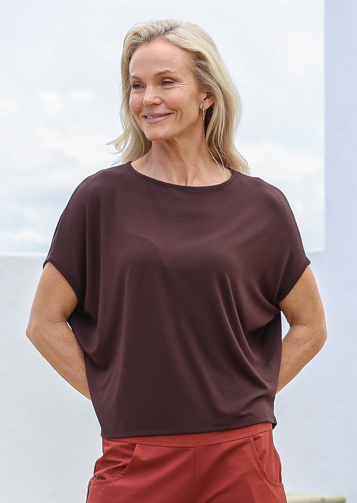 Woman wearing a brown top and red pants against a light background