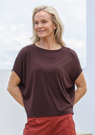 Woman wearing a brown top and red pants against a light background