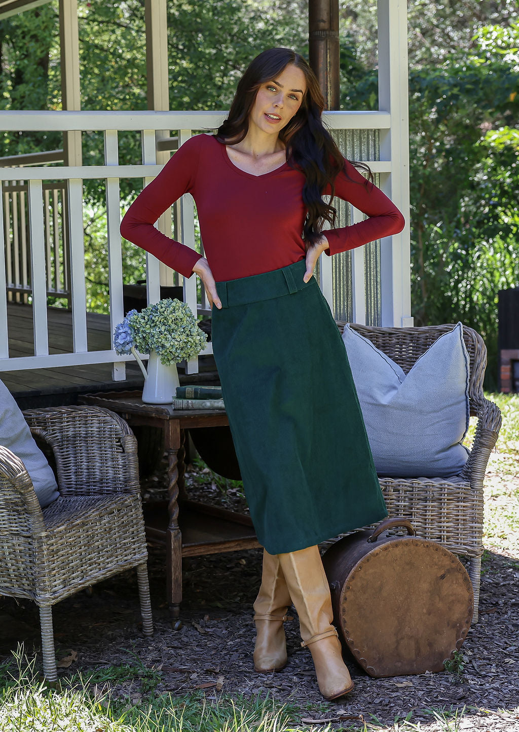 Woman in a green cotton corduroy A-line midi length skirt paired with a red long sleeve top and tan boots