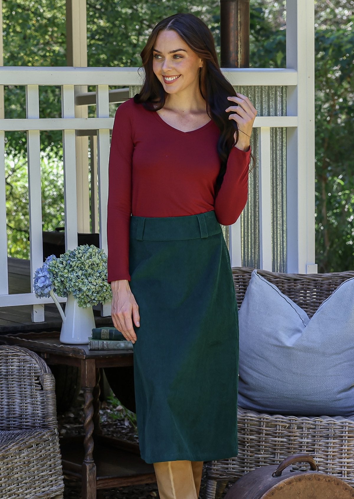 Woman in red top and green cotton corduroy A-line skirt standing outdoors with wicker chairs