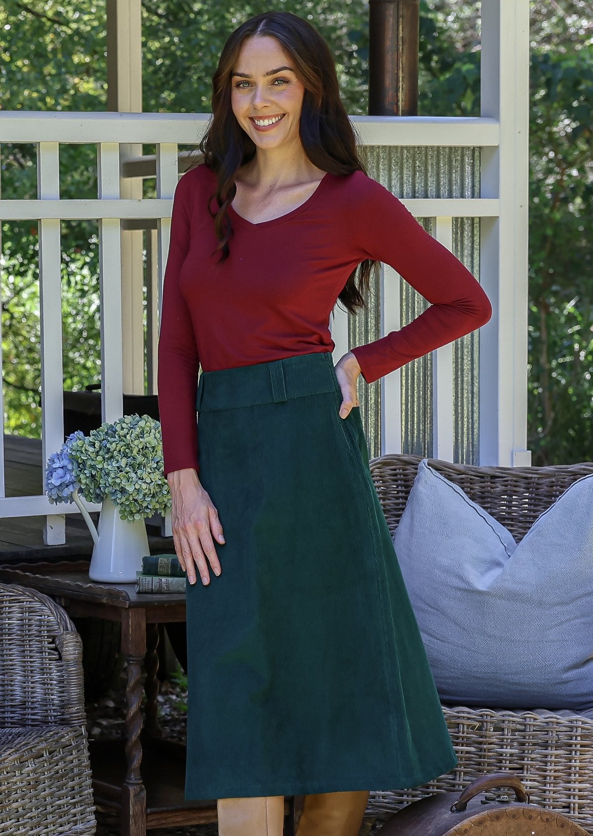 Woman in a red top and green cotton corduroy A-line midi length skirt paired with tan boots