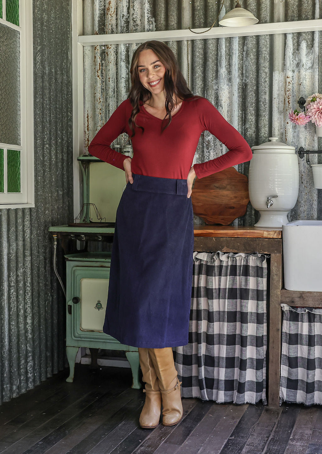 Woman in a red top and blue cotton corduroy midi length A-line skirt standing with hands on hips