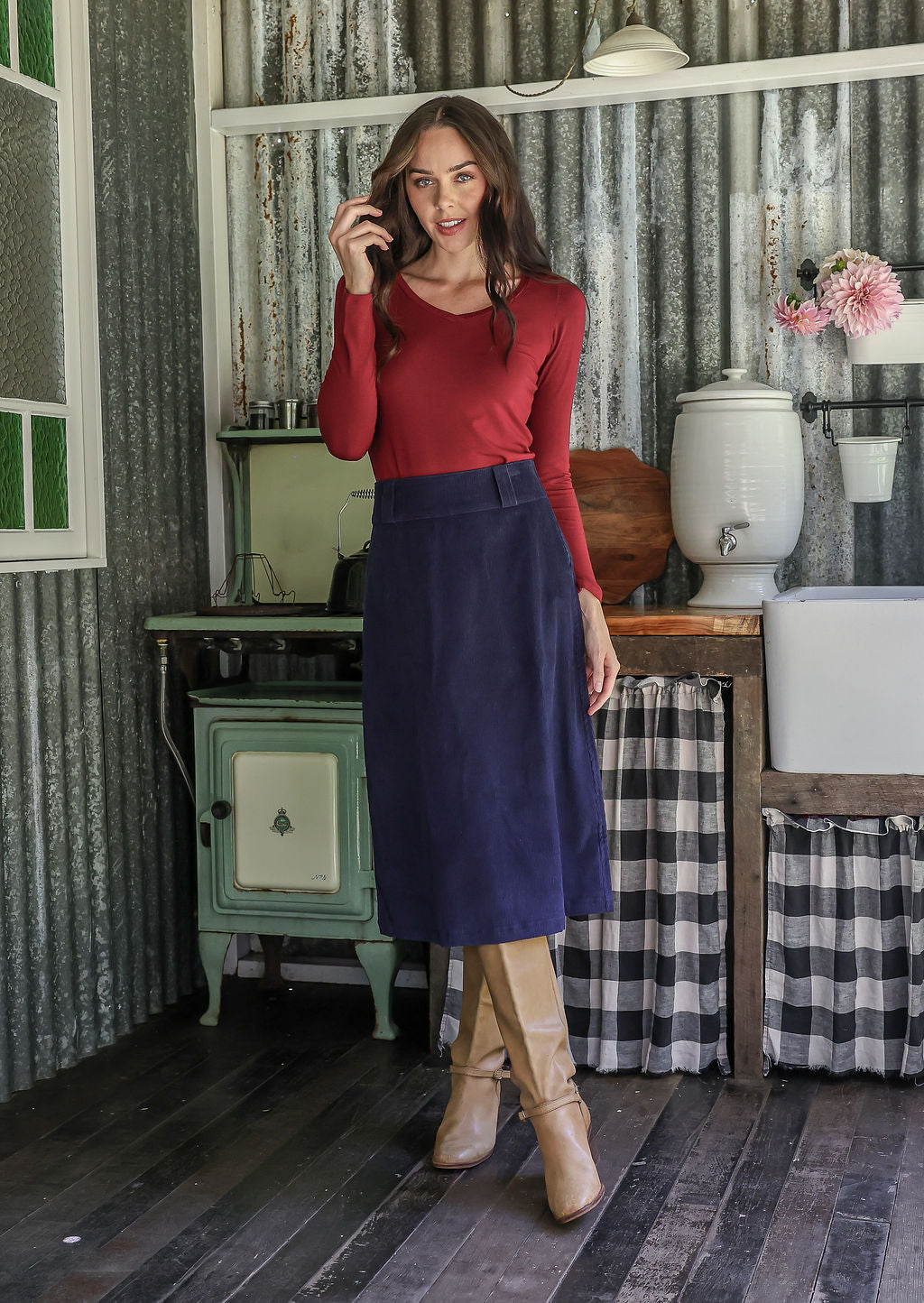Woman in a red top and blue cotton corduroy midi length skirt with belt loops, paired with tan boots