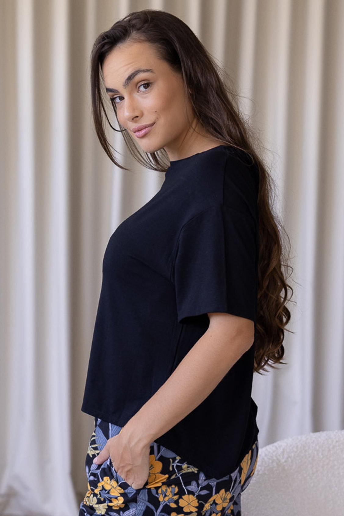 Woman wearing a black relaxed fit stretch rayon top with short sleeves and high round neckline with hands in pants pockets