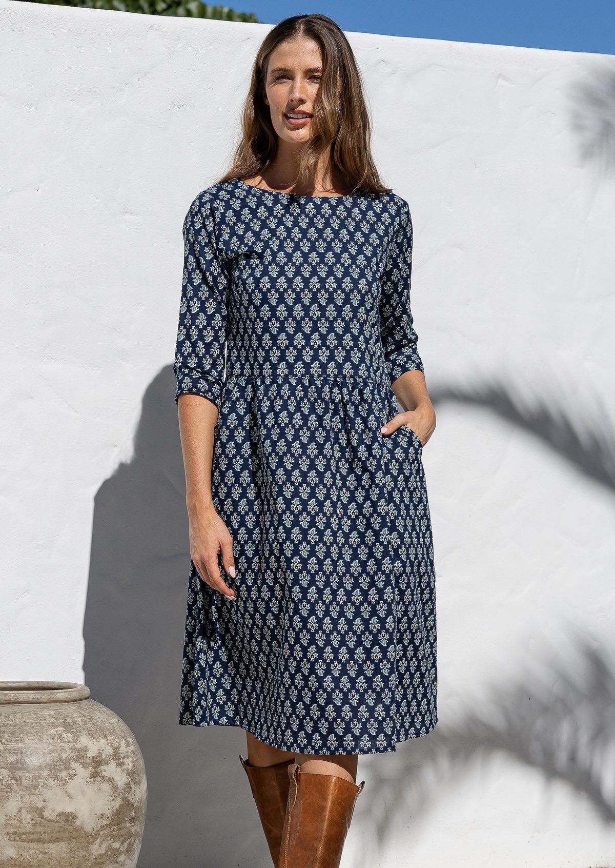 Model wears navy blue based knee length cotton dress with 3/4 sleeves, round neckline and one hand in pocket.