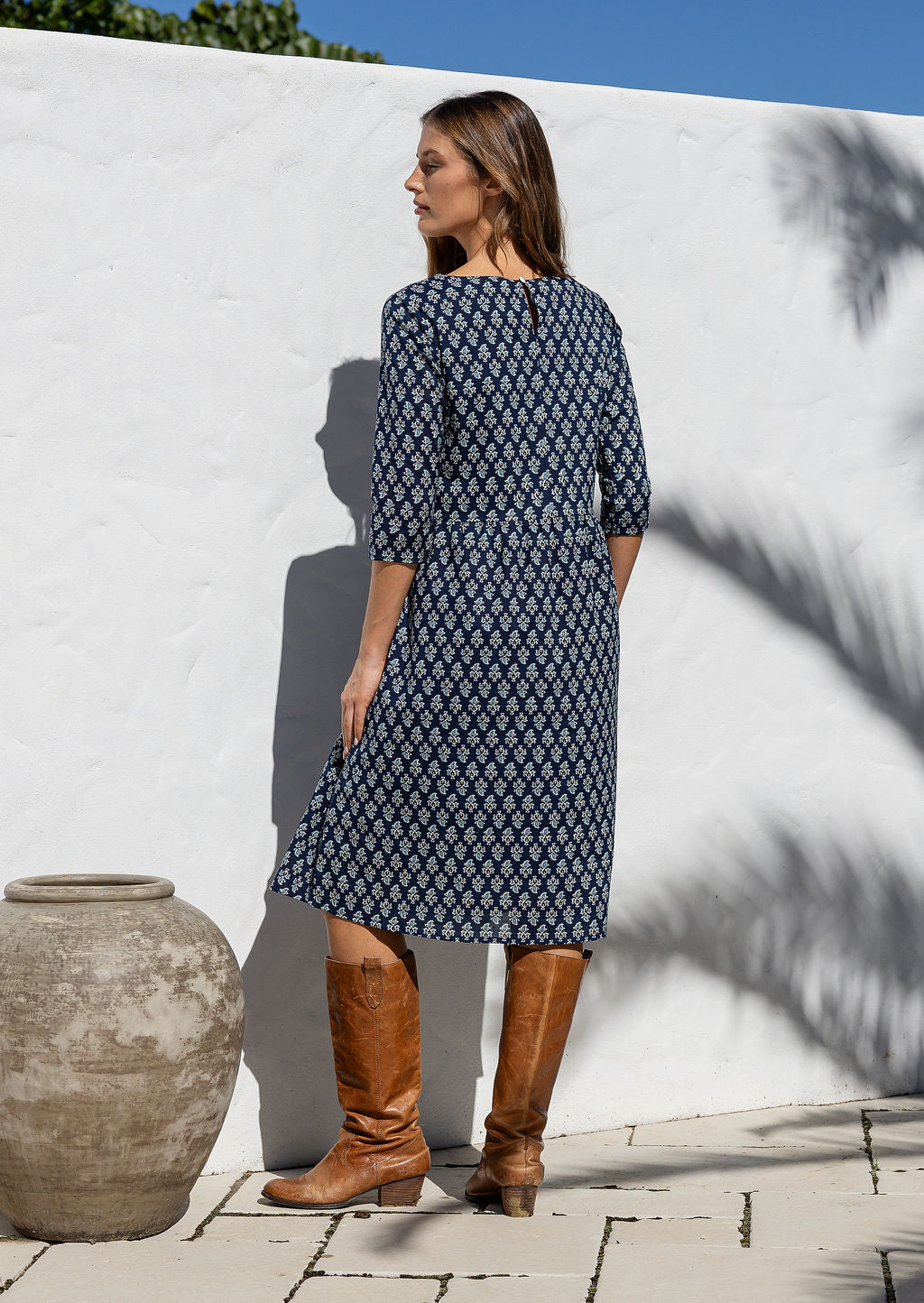 Model standing backwards wearing a relaxed fit cotton dress sitting just below the knee length in navy blue based floral print.