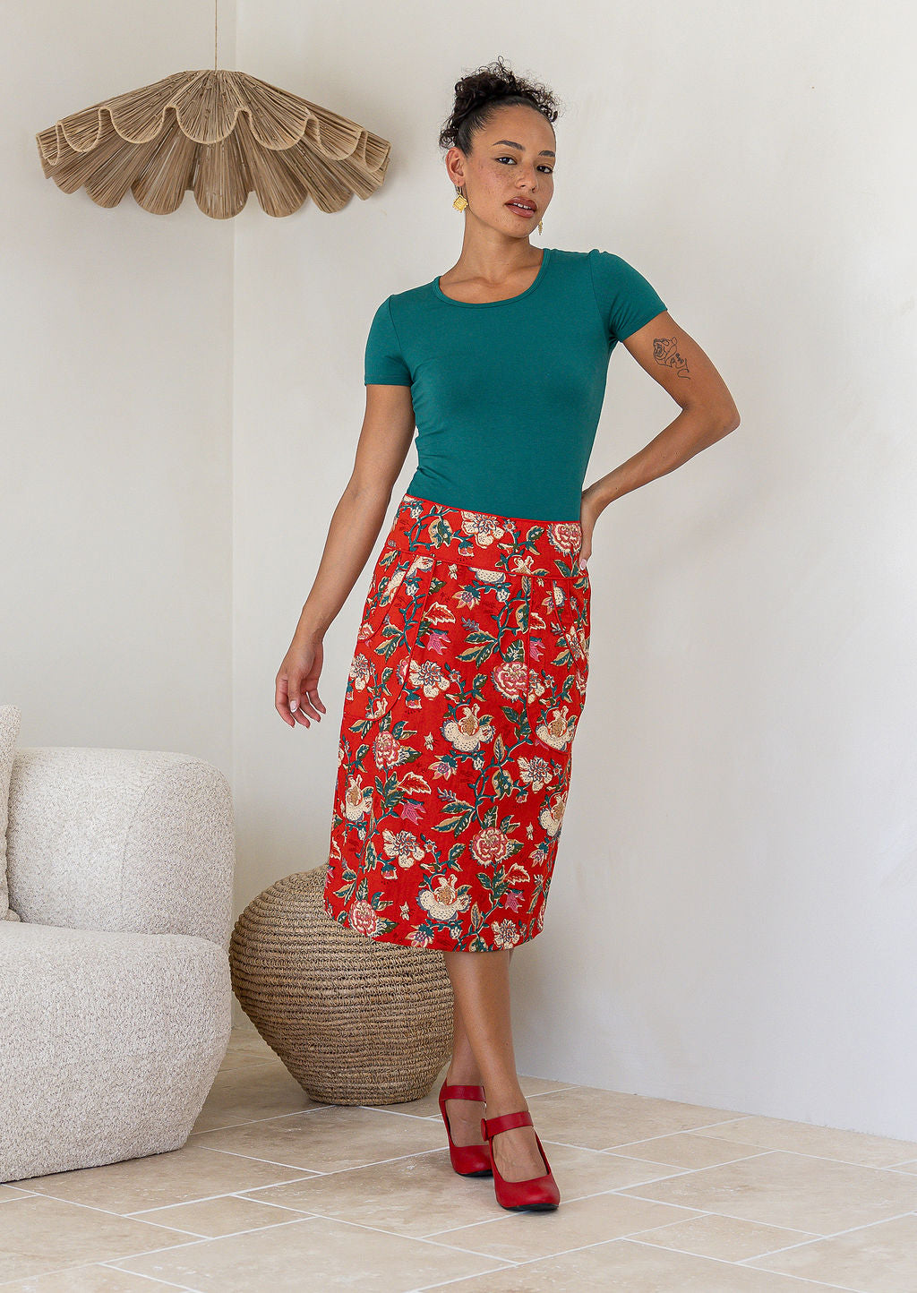 Woman wearing a high-waisted, knee length pencil skirt with piped detailing and pockets in a red based floral print.